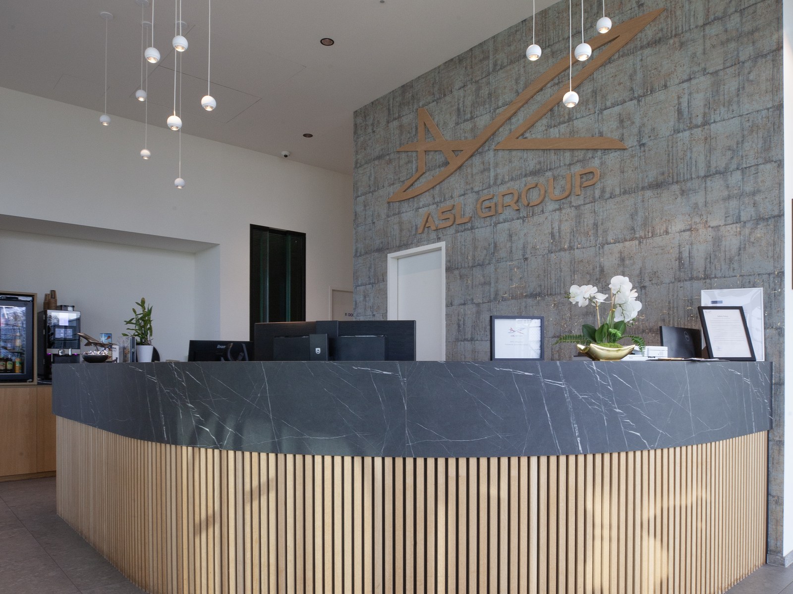 The reception desk of a private aviation terminal, with the ASL Group logo on the concrete wall behind it