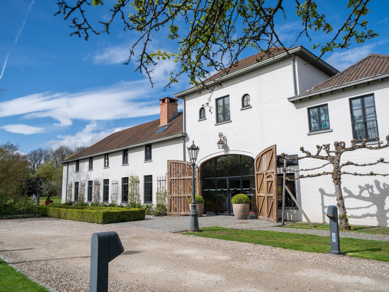 A white brick estate with an arched entrance and wooden gates, seen from the gravel drive