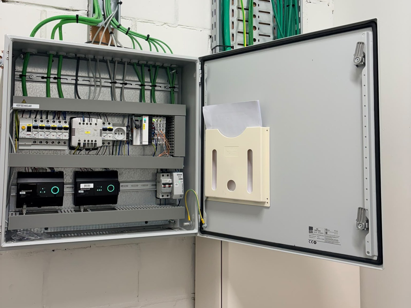 An open wall-mounted cabinet with a main switch, circuit protection and two meter interface units on the lower DIN rail
